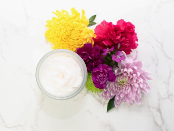 A white, floral shaped candle positioned next to a bouquet of colorful flowers on a marble surface